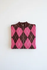 Campera de punto con cierre frontal, diseño de rombos en colores marrón y fucsia en el frente y mangas lisas de color marrón.