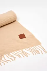 Pashmina de textura plisada en color beige, con flecos en el extremo inferior y un pequeño aplique de cuero sintético con logo grabado.