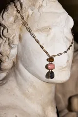 Collar largo de cadena eslabonada metálica dorada con un colgante compuesto por tres piezas de resina en tonos marrón, rosado y gris oscuro.