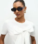 Remera de manga corta confeccionada en algodón, con cuello redondo y diseño recto. Presenta un lazo grande aplicado en la parte frontal que aporta volumen a la prenda.