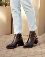 Botas de cuero negras con punta cuadrada, tacón ancho y detalles de textura en relieve en la parte superior.