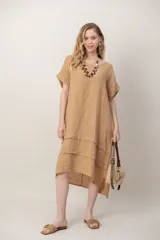 Vestido midi de lino color beige, de corte holgado y silueta acampanada. Cuenta con cuello redondo, mangas cortas amplias, bolsillos laterales y detalles de recortes horizontales en la falda con terminación asimétrica más larga en la parte trasera.
