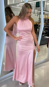 Vestido largo rosado de satén, con escote halter alto y espalda descubierta. Presenta un tajo pronunciado en la pierna izquierda y diseño drapeado en los laterales.