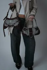 Bolso bandolera de cuero color borravino y tela a cuadros príncipe de Gales. Tiene correa ajustable, cierre metálico plateado y herrajes plateados.