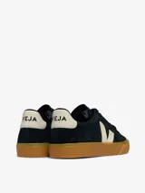 Championes Veja modelo Campo, confeccionados en gamuza negra con el logo lateral y detalle en el talón en color crema. Presentan suela de goma color caramelo y cierre con cordones negros.
