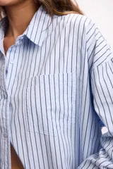 Camisa de corte oversize con estampado de rayas verticales, cuello clásico, cierre frontal con botones y bolsillo aplicado en el pecho.