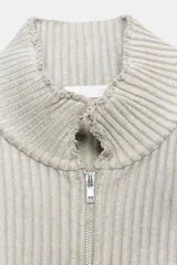 Top chaleco de punto acanalado con efecto lavado, cuello subido, cierre frontal con cremallera y bolsillo de plastrón en el delantero. Presenta un diseño sin mangas con bajo asimétrico.
