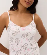 Pijama short doll de dos piezas en color blanco con estampado de ositos cariñositos y estrellas rosadas. Está compuesto por una musculosa de escote en V con tirantes finos y detalle de moño, y un short con cintura elástica y bordes ondulados.