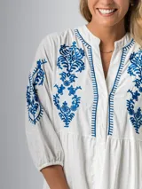 Vestido corto blanco de algodón italiano con bordado azul, mangas tres cuartos y botones frontales. Tiene forro interior en la falda.