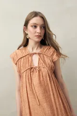 Vestido largo con estampado geométrico en tonos azul, marrón y beige. Tiene escote en V con lazos ajustables, mangas cortas y corte holgado.