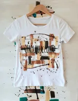 Remera blanca de manga corta y cuello redondo, con diseño artístico estampado en tonos dorados, marrones y negros con la firma Carolina De Cunto.