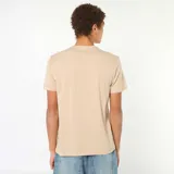 Camiseta de algodón color beige con cuello redondo y mangas cortas. Presenta un estampado frontal en color verde oscuro con la inscripción '90/L.A. CALIFORNIA' y el texto 'FROM THE BLOCK TO THE BEACH'.