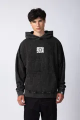 Buzo canguro con capucha, de calce oversize y efecto lavado gastado. Presenta un estampado gráfico central en color blanco y un pequeño parche con logo en el puño.