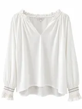 Blusa blanca de manga larga con cuello en V, detalles fruncidos en el escote y puños elásticos con bordados decorativos.