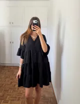 Vestido corto negro con escote en V, botones frontales y mangas cortas con volados. La falda es de corte acampanado con volados en capas.