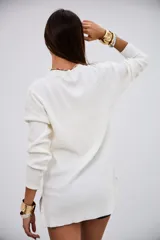 Sweater de punto acanalado color blanco, con cuello en V y mangas largas. Presenta un diseño de corte recto y largo tipo túnica con aberturas laterales en el ruedo.