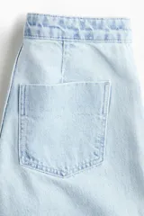 Jean de denim de algodón rígido, de color celeste claro, con tiro alto y pierna amplia de corte extraholgado. Presenta diseño clásico de cinco bolsillos, cierre frontal con cremallera y botón metálico.