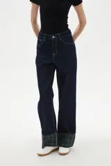 Pantalón de jean azul oscuro de corte recto y tiro alto, con costuras en contraste y dobladillo con vuelta que revela un estampado de cuadros en tonos verdes y azules.