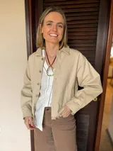 Campera de gabardina color beige, con diseño liso, cuello camisero, cierre frontal con botones metálicos y ruedo con detalle de flecos deshilachados.