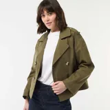 Trench corto de color verde militar, con diseño de doble botonadura, solapas anchas y trabillas en los hombros. Presenta un corte estructurado y mangas largas.