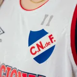 Musculosa de básquetbol Umbro del Club Nacional de Football, color blanco con detalles en azul y rojo en cuello y sisas. Presenta el logo de la marca y el escudo del club en el pecho, junto con la inscripción Nacional en letras grandes.