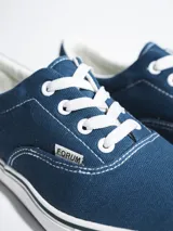 Championes de lona color azul grisáceo, estilo skate o casual, con cordones blancos y suela de goma blanca con una línea fina azul en el borde.