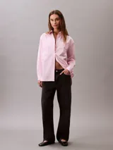 Camisa de corte relaxed confeccionada en popelina de algodón con elastano. Presenta cuello de punta clásico, cierre frontal con botones, mangas largas y un bolsillo en el pecho con el monograma CK bordado en relieve.