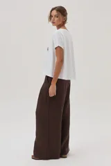 Remera blanca de algodón con cuello bote y manga corta, con un estampado central que incluye dos palmeras reflejadas y la palabra "SUNRISE" bordada en el centro.