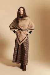 Poncho de silueta amplia y caída fluida, color beige con detalles de líneas en contraste color marrón en los bordes.