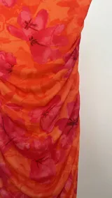 Vestido corto de microtul con diseño drapeado, escote strapless y estampado floral en tonos naranja y fucsia.