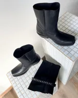 Botas de cuero vacuno color negro, con diseño versátil que incluye una polaina desmontable y un estribo decorativo con tachas metálicas. Presentan un taco bajo y punta redondeada.