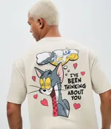 Remera de algodón color beige con cuello redondo y mangas cortas, con estampa en la espalda del personaje Tom de Tom y Jerry junto con la frase "I've been thinking about you" y corazones.