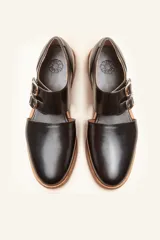 Zapato tipo oxford abierto en los laterales, confeccionado en cuero vacuno negro. Presenta doble tira con hebillas metálicas en el empeine y detalle de tachas plateadas en el contorno del talón y la puntera.