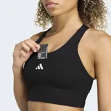 Sujetador deportivo Adidas de sujeción media, color negro, con escote redondo y espalda de nadador. Presenta un logo de tres barras blancas en el centro del pecho y una banda ancha elástica inferior.