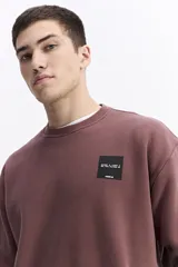 Buzo de algodón con calce oversize, cuello redondo, mangas largas con puños y bolsillos laterales. Presenta un parche cuadrado negro con lettering en el pecho y detalle de estampado en el ruedo.