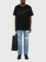 Remera de algodón negra de corte clásico, con cuello redondo y mangas cortas. Presenta el logo de la marca Balmain bordado en relieve en el frente.