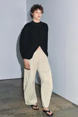 Top corto negro de punto fino, con cuello redondo y mangas largas abullonadas con pliegues.