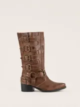 Bota de caña alta estilo biker, color marrón, con punta redondeada y taco cuadrado. Presenta múltiples tiras horizontales con hebillas metálicas y detalles de herrajes en el lateral. Confeccionada en cuero con forro vacuno y suela de madera.