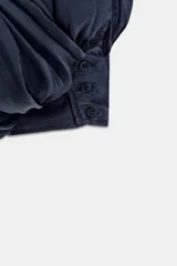 Mono largo satinado de color azul marino, con cuello halter, escote en V profundo y espalda descubierta. Presenta diseño plisado y bajo abullonado con terminación en puño.