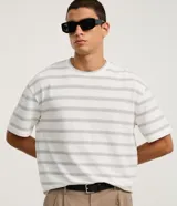 Remera de corte boxy con cuello redondo y mangas cortas. Presenta un diseño de rayas horizontales finas en tonos gris sobre fondo blanco.