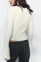 Jersey de punto pointelle color blanco, con cuello redondo y mangas largas acabadas en evasé.