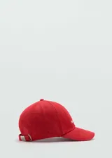 Gorra de béisbol color rojo, confeccionada en algodón con textura tipo denim. Presenta un mensaje bordado en el frente y cierre metálico ajustable en la parte posterior.