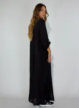 Vestido largo tipo camisero de color verde oliva, con cuello clásico, cierre frontal completo con botones y mangas largas con opción de arremangar. Presenta un corte holgado y fluido.