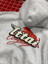Buzo con capucha gris jaspeado, de corte holgado, con estampado gráfico en la espalda que incluye el texto 'Ittai Company' y una figura de un animal en color rojo.