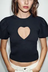 Jersey de punto negro con cuello redondo y mangas cortas abullonadas. Presenta una abertura frontal en forma de corazón.