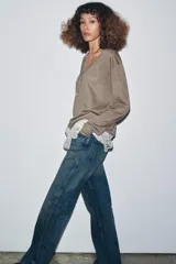 Jersey de punto fino en color marrón topo con escote en pico y manga larga. Presenta un diseño de doble capa con un bajo de encaje floral en color crudo que sobresale en la parte inferior.