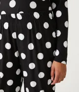 Pijama de dos piezas con estampado de lunares blancos sobre fondo negro. Incluye una blusa de manga larga con cuello redondo y un pantalón largo con cintura elástica y cordón ajustable.