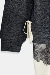 Vestido de cuello redondo y manga larga, confeccionado en tejido de punto gris oscuro. Presenta un bajo en contraste de color beige con detalle de encaje floral negro y lazada lateral ajustable.