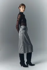 Falda midi de denim rígido con lavado gris, presenta cierre frontal con botones metálicos grabados y diseño de recortes verticales en el frente.