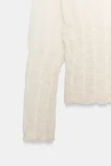Jersey de punto semitransparente color crudo con cuello redondo y mangas largas, con detalles de nido de abeja elástico en el cuerpo y los puños.